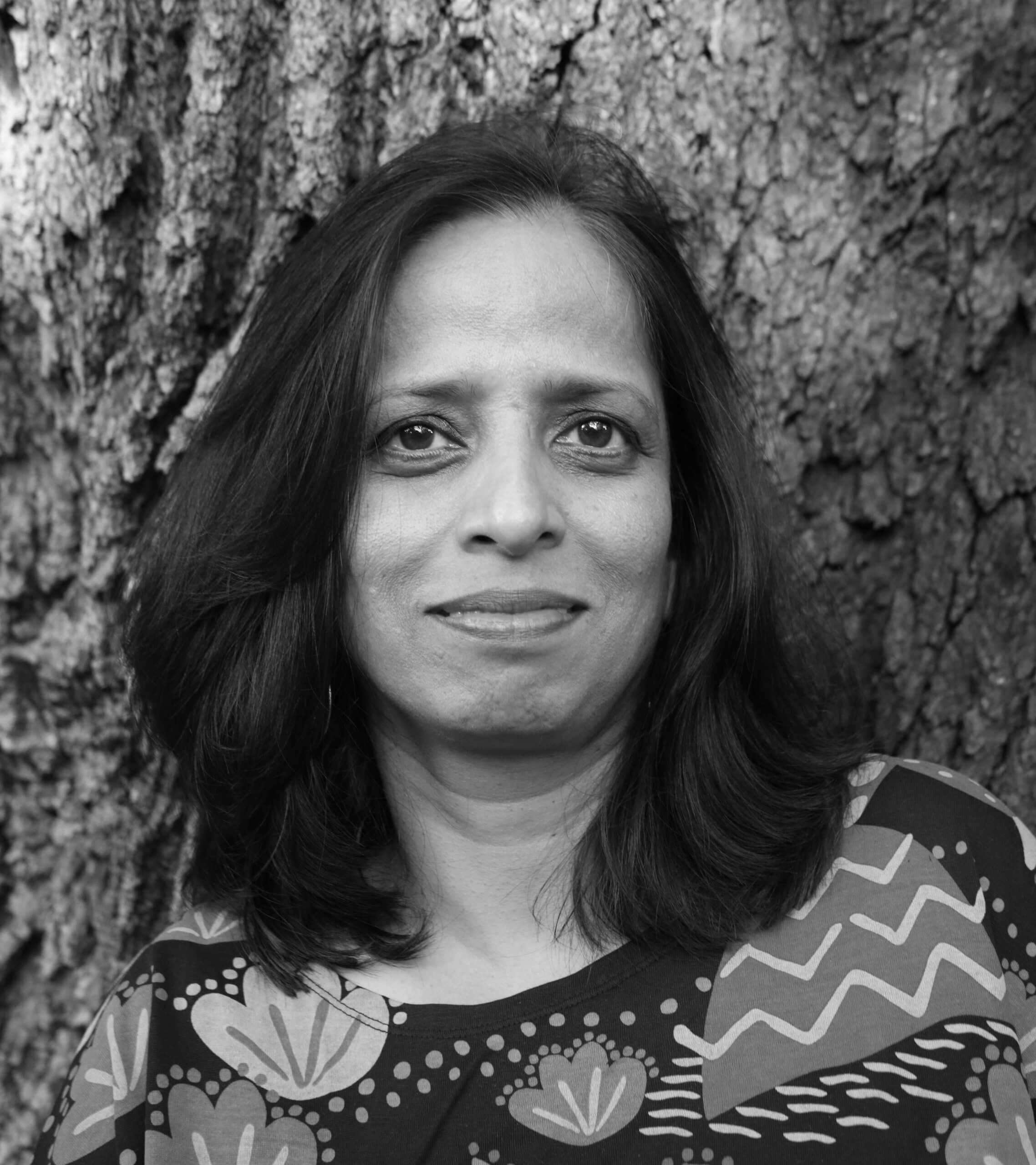 Nistha Jain stands in front of a tree. She has shoulder-length dark hair and wears a patterned blouse. Black and white portrait.