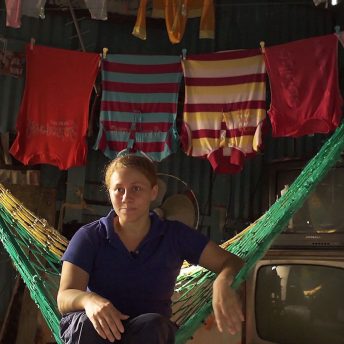 Still from Once Upon a Time in Venezuela. A woman sits in a hammock with TVs and shirts hanging on a clothing line behind her.