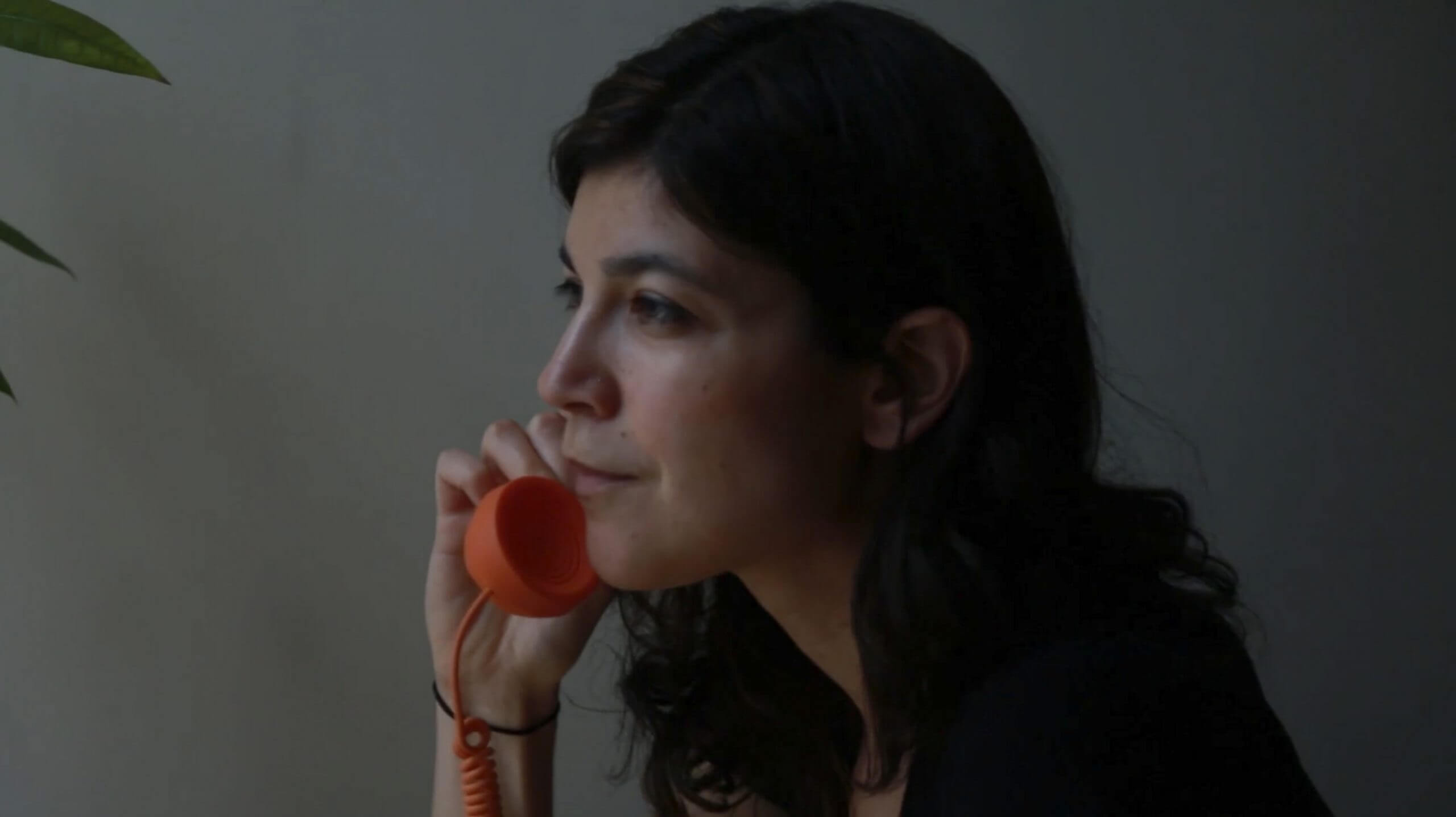 Still from A Photographic Memory. Profile shot of Rachel Elizabeth Seed with an orange corded phone on her ear.
