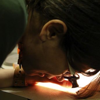 Still from A Photographic Memory. A woman is using a special magnifying glass to see a photograph on a light table.