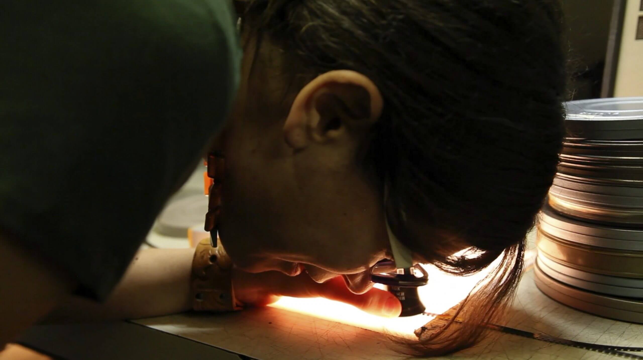 Still from A Photographic Memory. A woman is using a special magnifying glass to see a photograph on a light table.