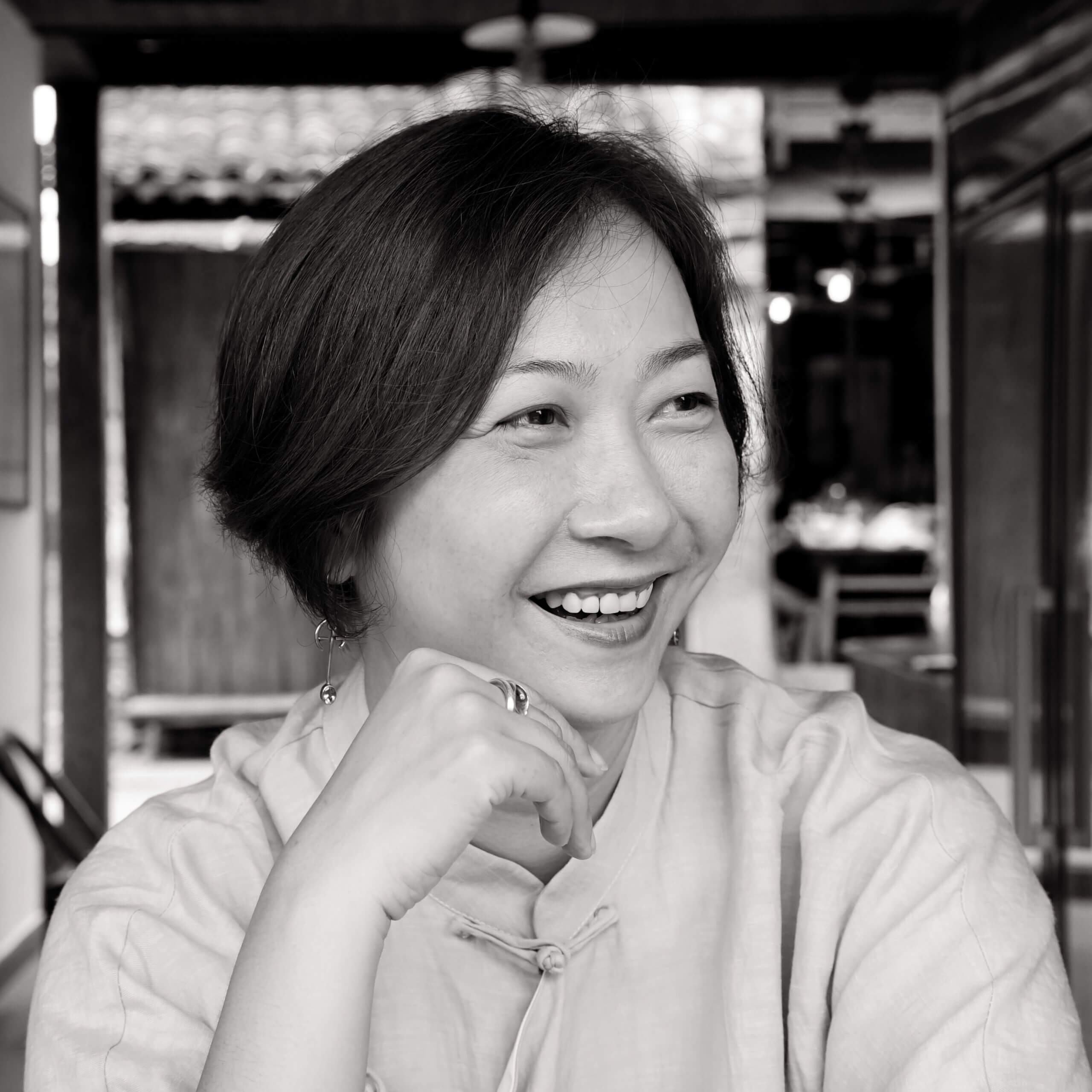 Qing Zhao looking to her side and smiling. She has short dark hair, and is wearing a light-colored blouse. Black and white portrait, with out of focus background.