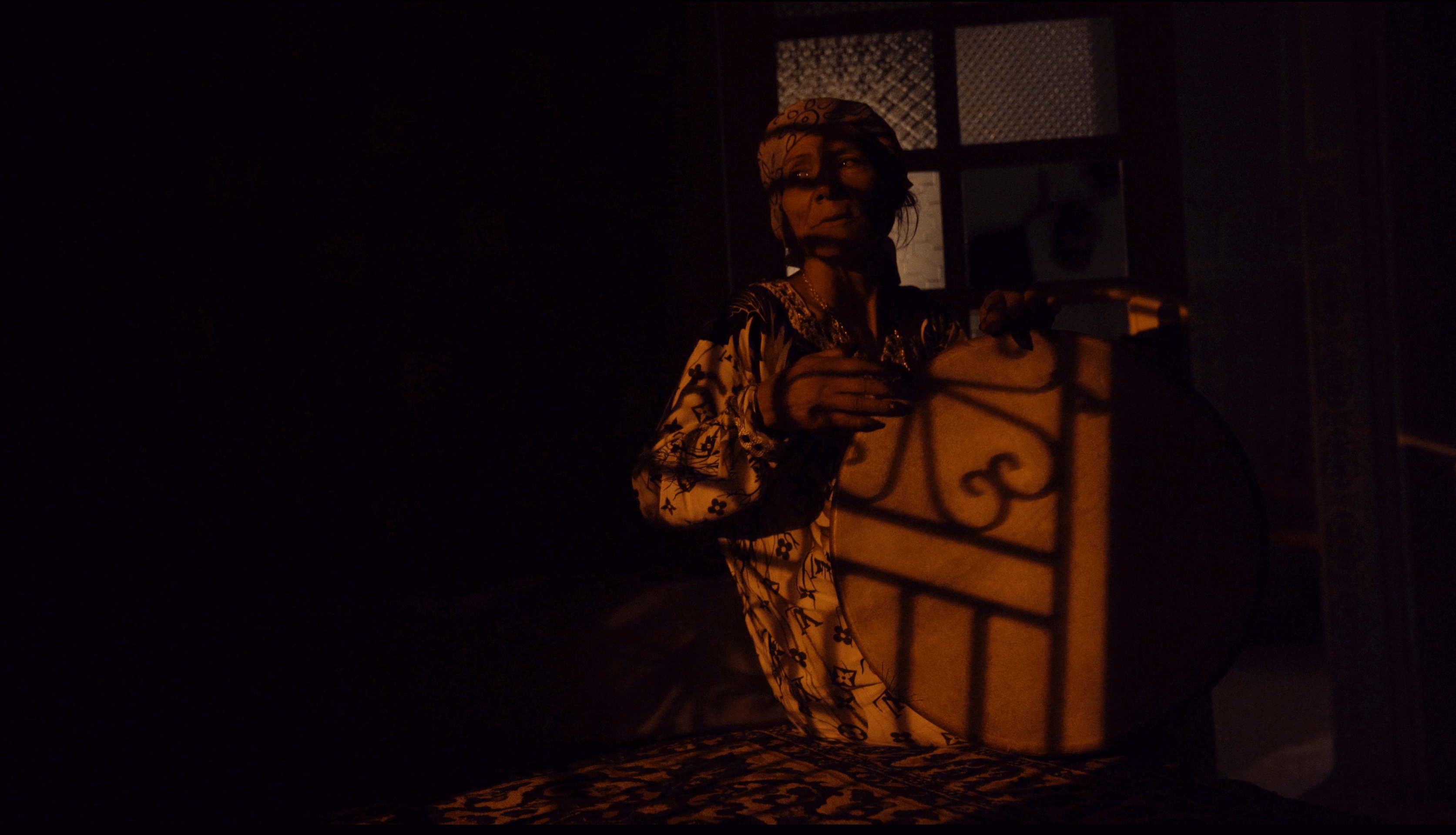 Still from Machtat. A woman sits in a dark room playing a drum.