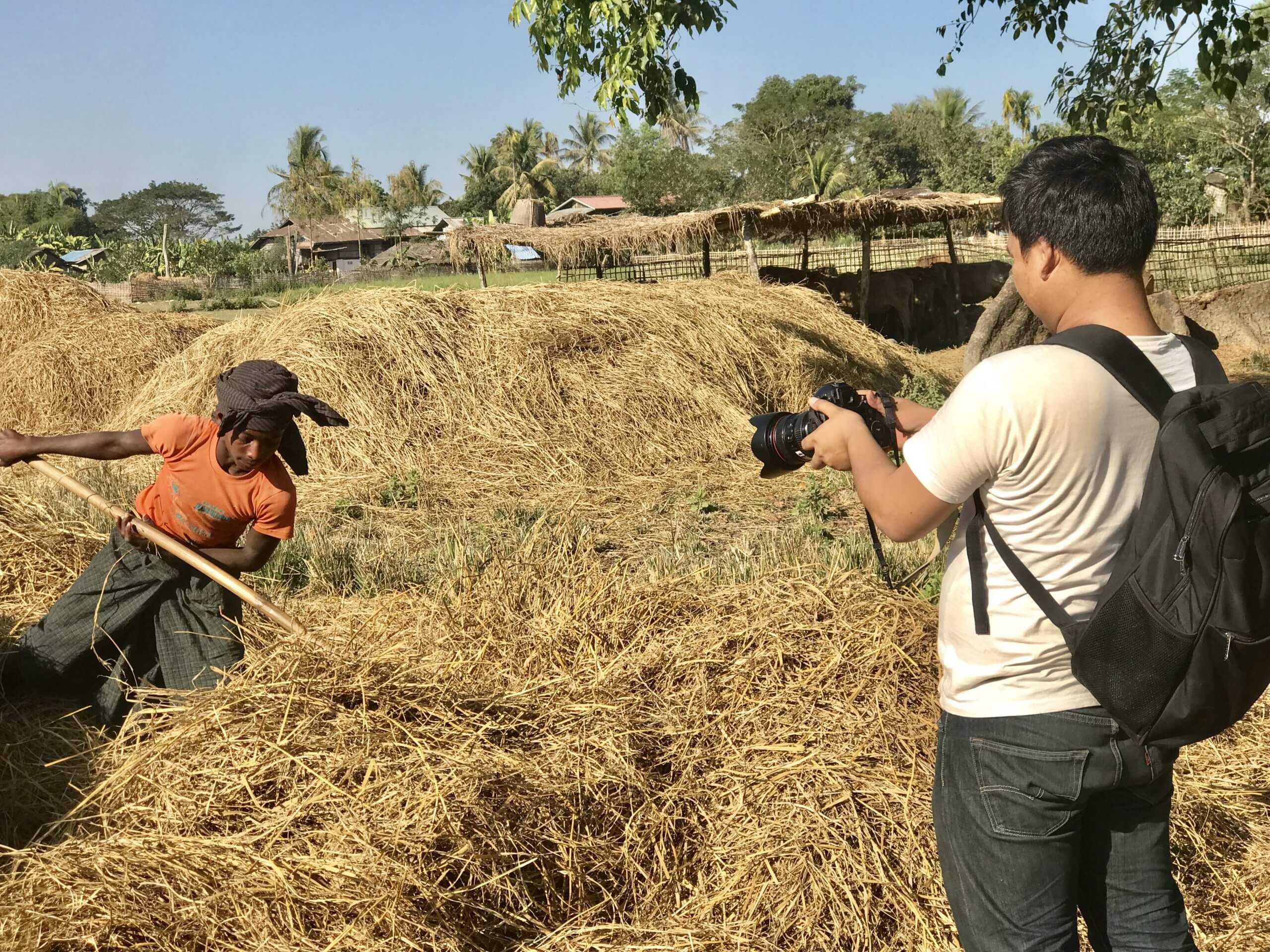 Production still from Midwives. A camera man wearing a backpack is taking video of a young boy moving hay.