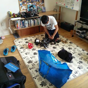 Production still from All of Our Heartbeats Are Connected Through Exploding Stars. A camera person on the floor setting camera equipment ready. They are inside of a living room.