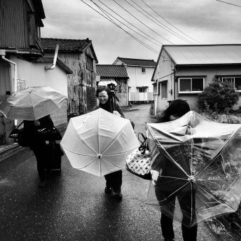 Production still from All of Our Heartbeats Are Connected Through Exploding Stars. The people from the crew are walking with umbrellas and equipment. Black and white shot.