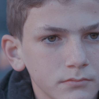 A close-up shot of a boy looking off into the distance. He has short brown hair and brown eyes.