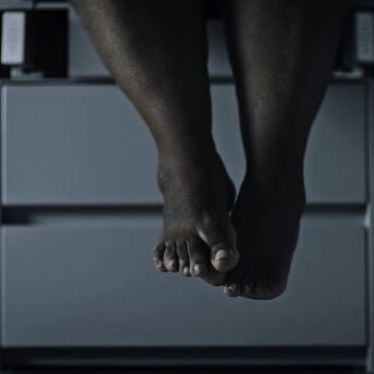 Still from Belly of the Beast. Feet dangling on an exam table.
