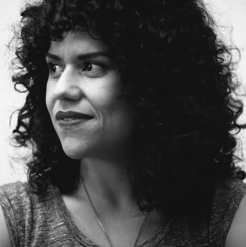 Cecilia Aldarondo is looking away from the camera. She has medium curly hair and is wearing lipstick. Portrait in black and white.