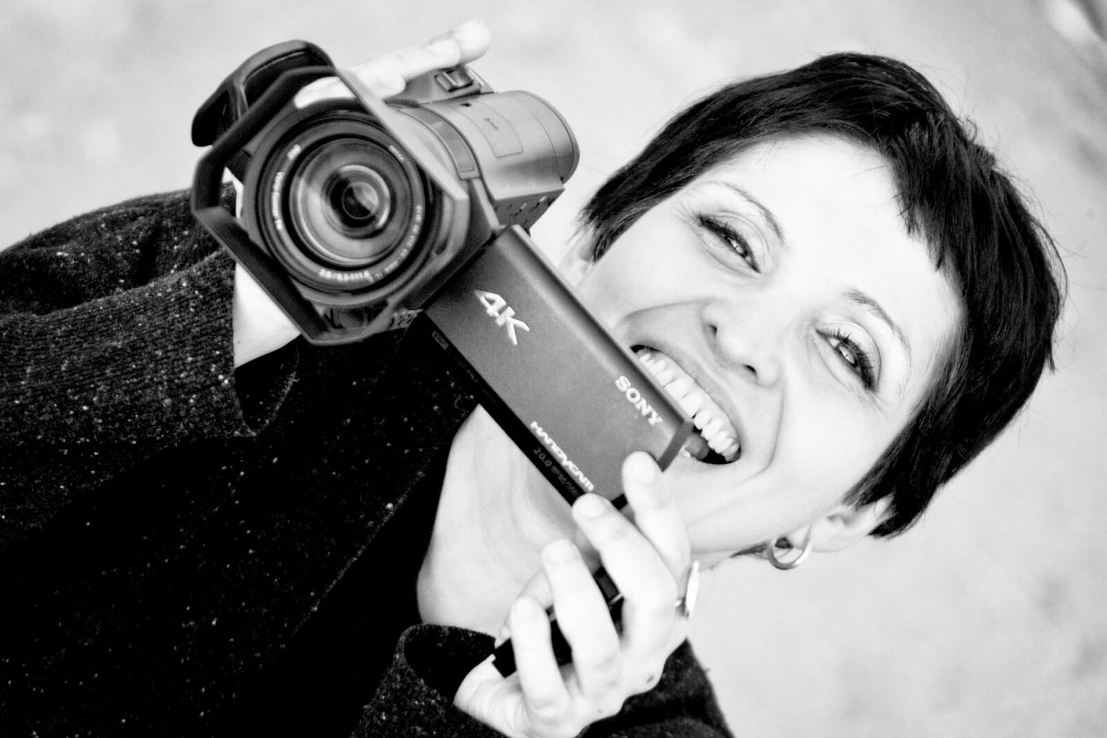 Maryam Ebrahimi is behind a Sony 4K camera, smiling. Black and white portrait.