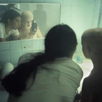 Production still. Tatiana Huezo and a child are in front of a mirror. Tatiana is holding a light meter in front of the child's eyesight.
