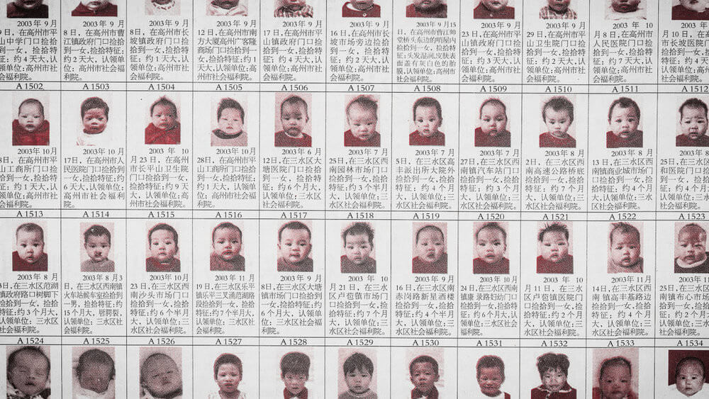 Still from One Child Nation. Photograph of a printed graphic of a grid with pictures of infants and text in Chinese.