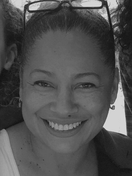 Selina Davidson smiling at the camera. She wears her eyeglasses on top of her head. Her hair is pulled back on her head. Portrait in black and white.