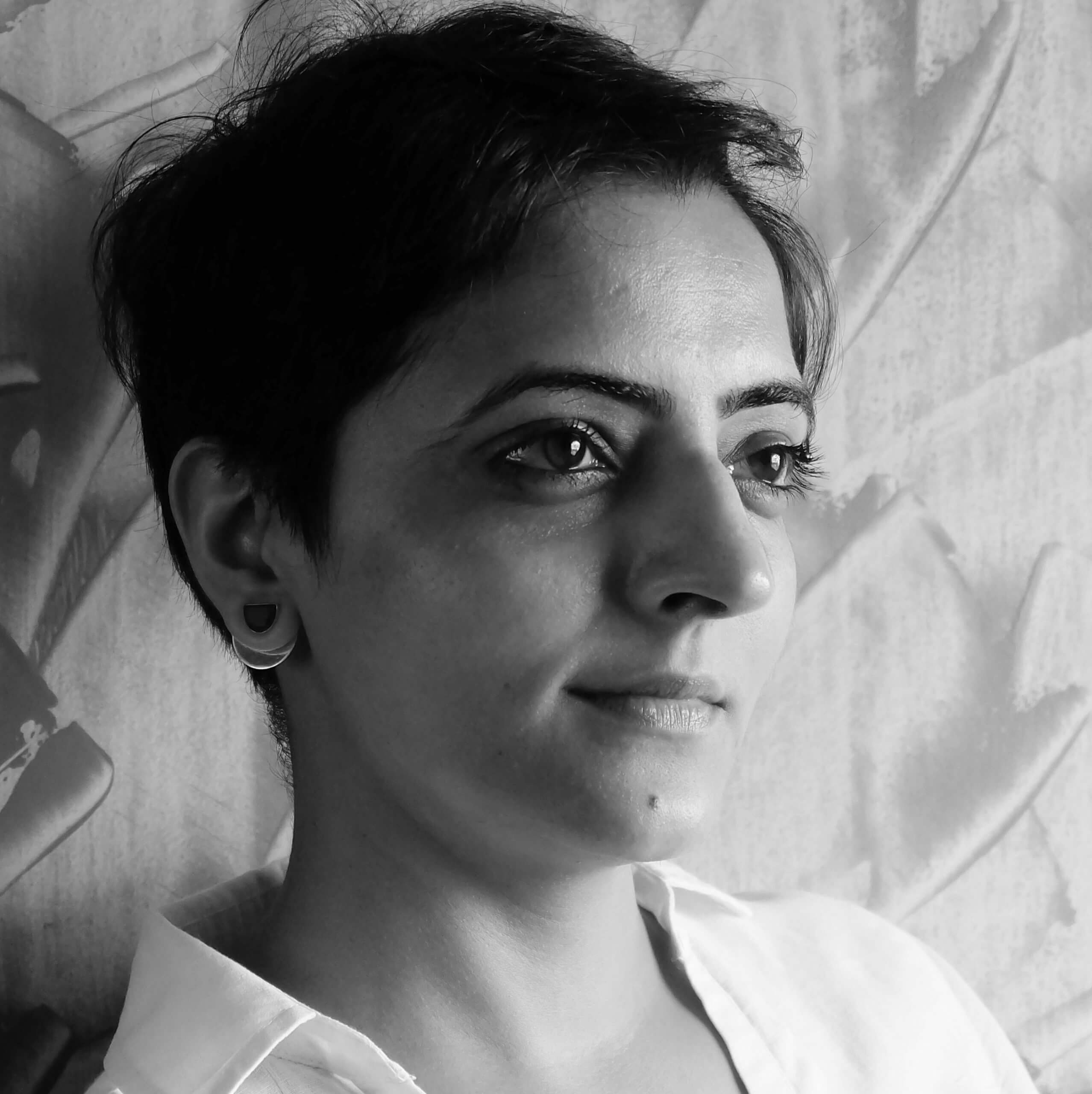 Sarvnik Kaur is leaning against a paper wall and looks away from the camera. She has short hair, and wears a shirt. Portrait in black and white.