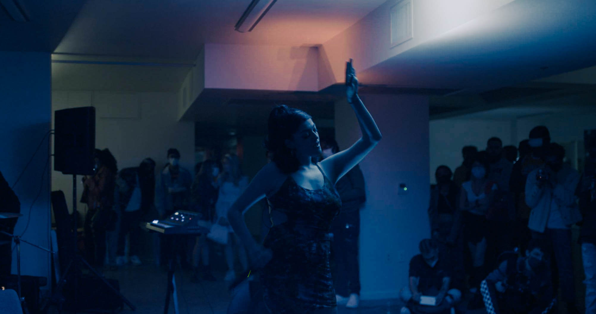 Still from Mija. A woman dances in a dark room surrounded by others.