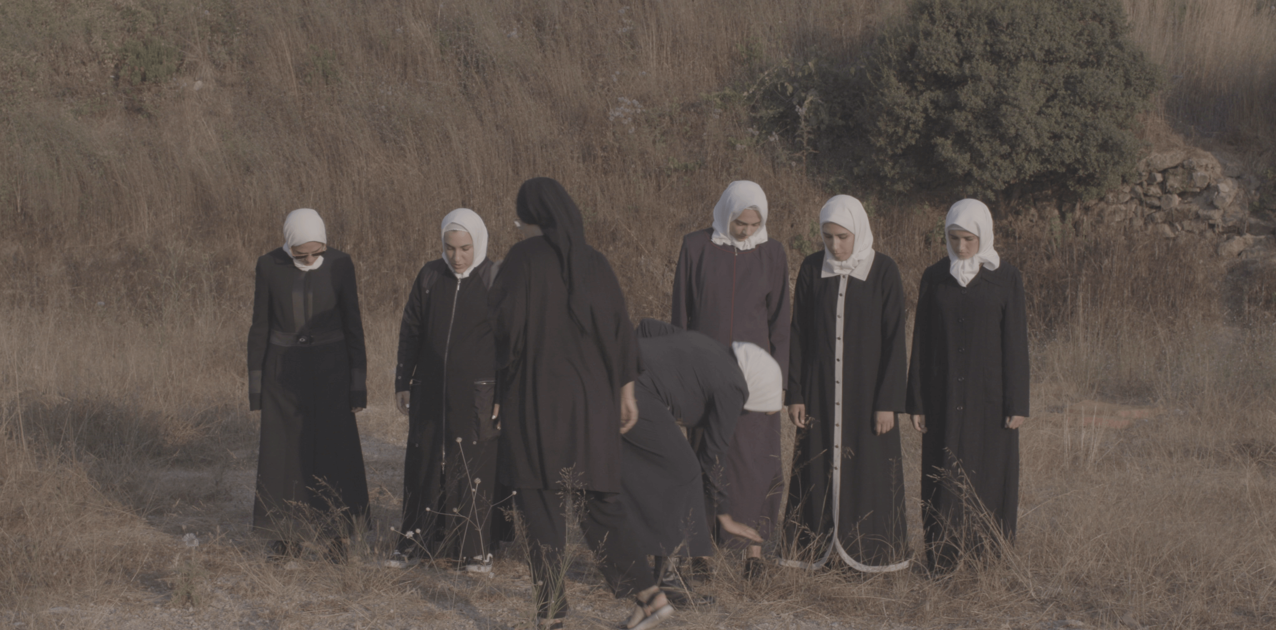 Still from Q. Seven women wearing hijabs in a field.