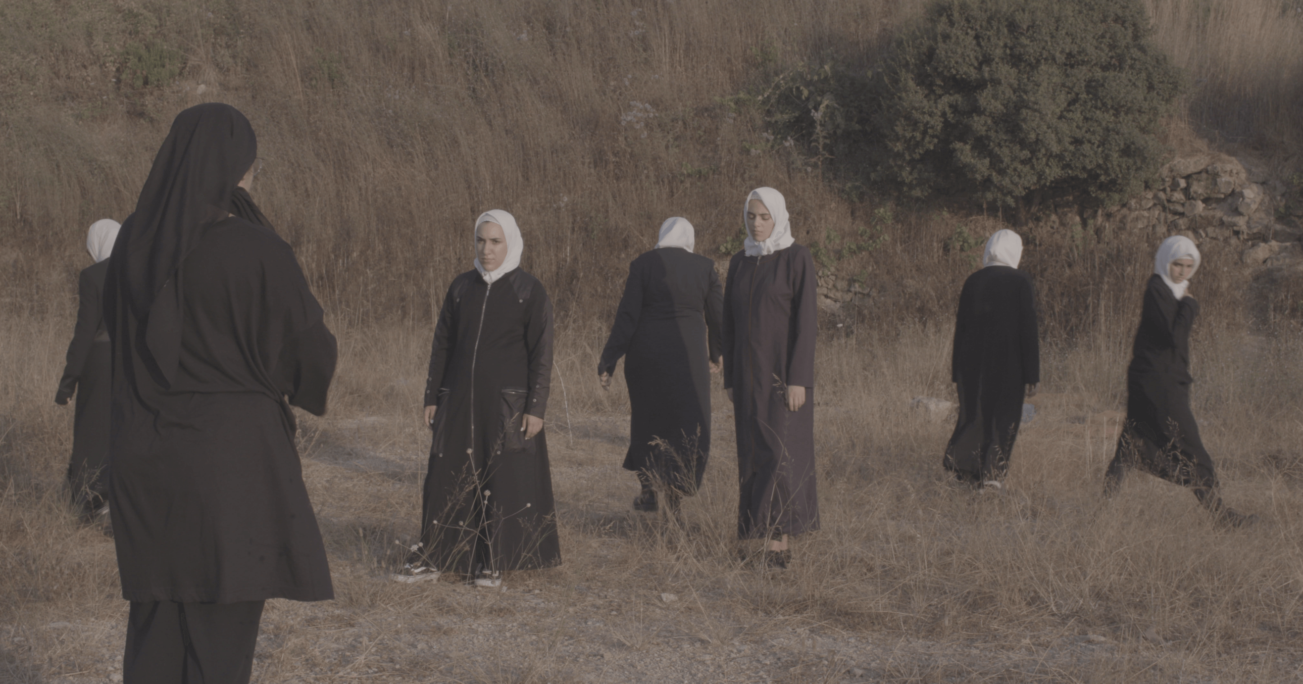Still from Q. Seven women wearing hijabs walk around in a field.