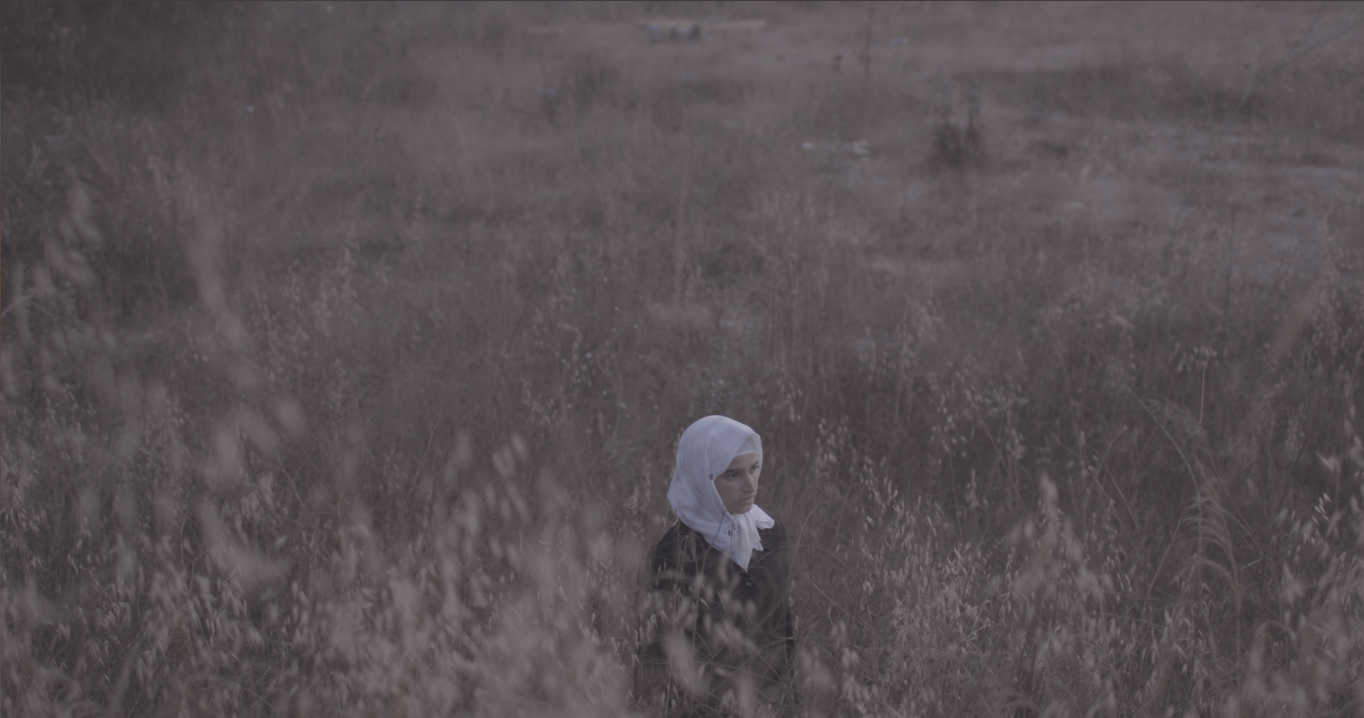 Still from Q. A woman wearing a hijab is walking through a field.