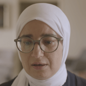 Still from Q. Close-up of a woman wearing glasses and a hijab. She has a tear on her left cheek.