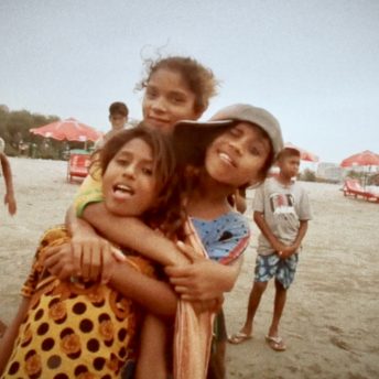 Still from Bangla Surf Girls. Three young girls on the beach are hugging in front of the camera.