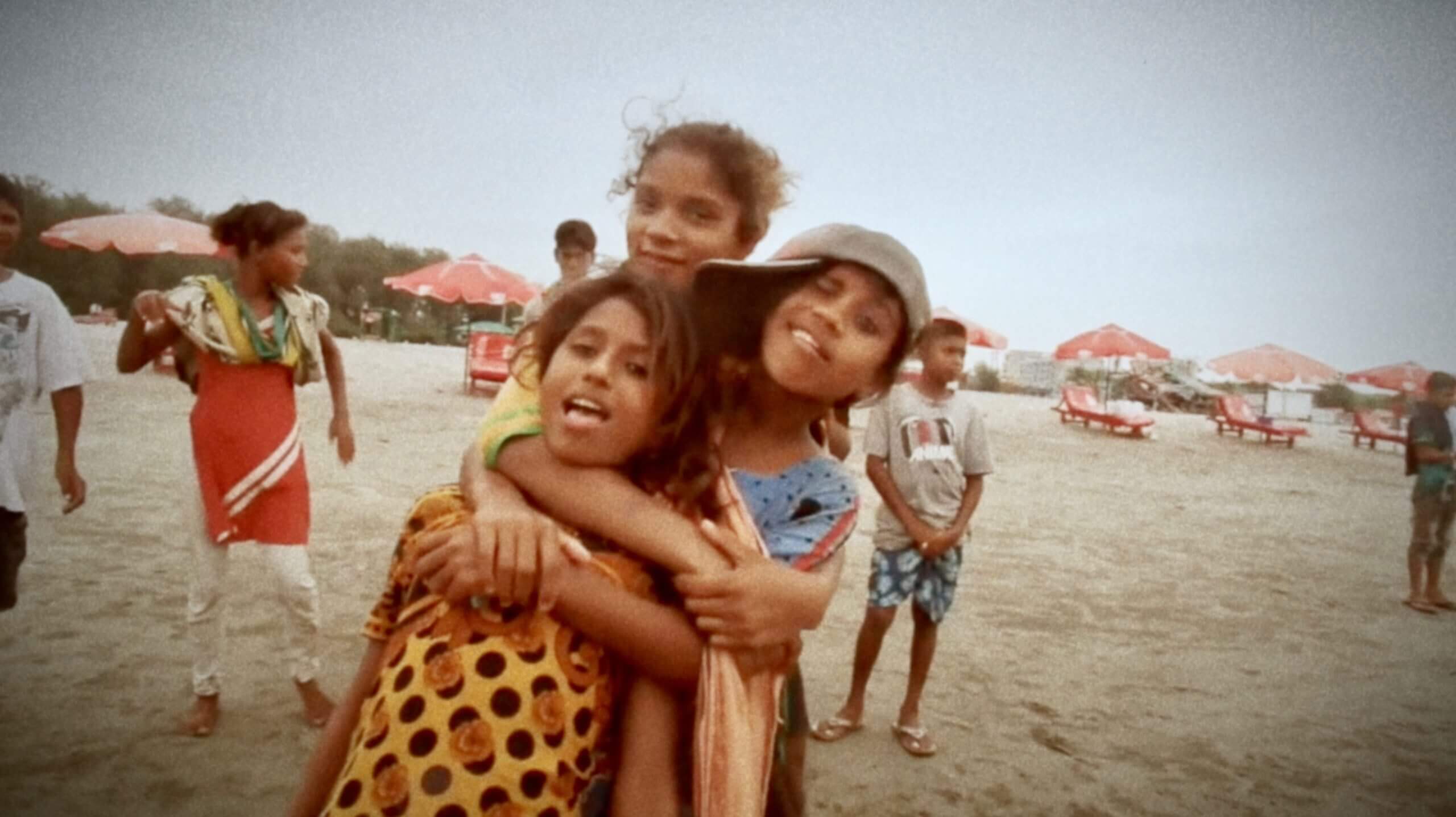 Still from Bangla Surf Girls. Three young girls on the beach are hugging in front of the camera.