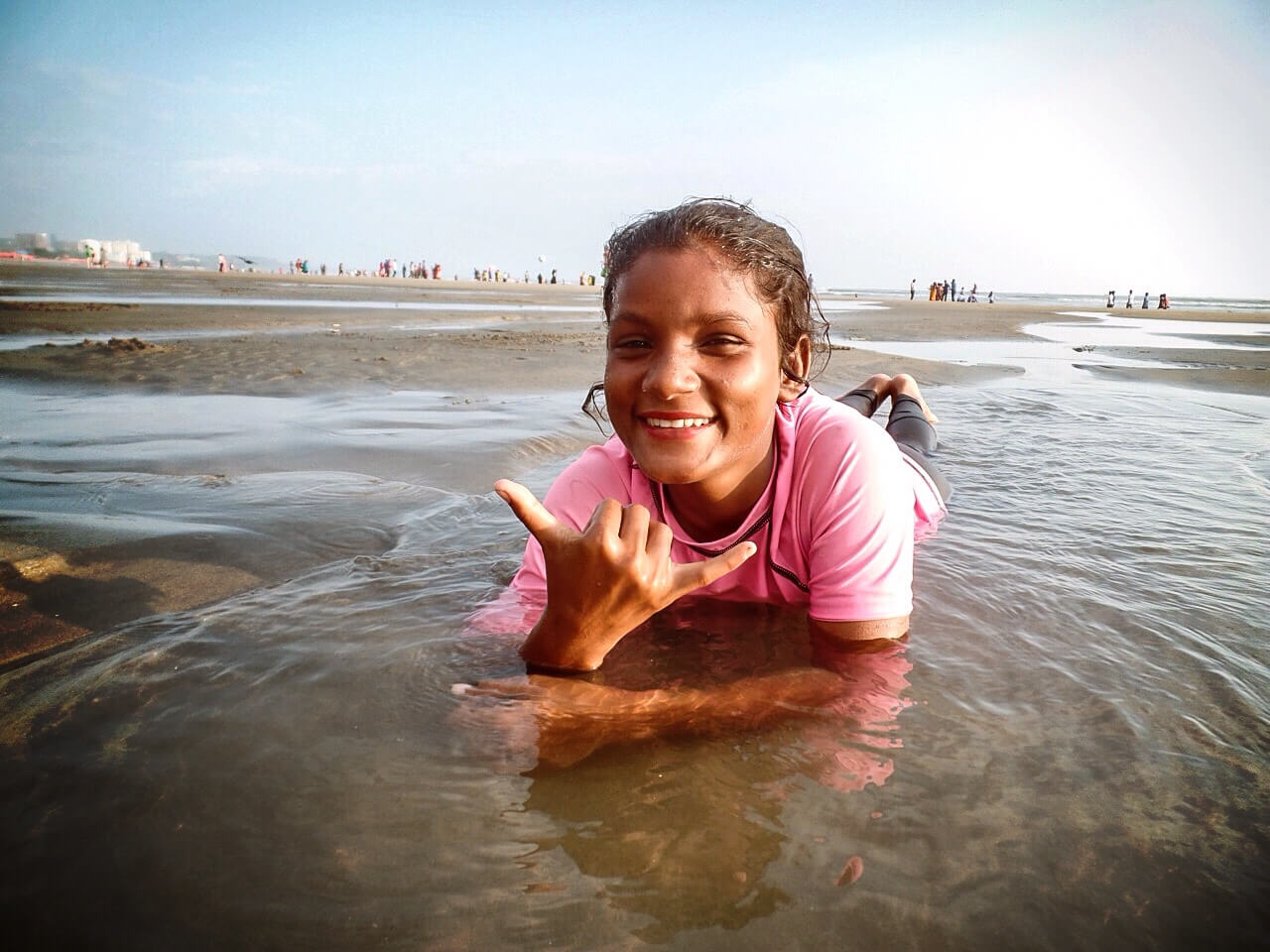 Still from Bangla Surf Girls. A young girl is lying on the seashore, she is smiling at the camera and is partly being covered by the ocean.