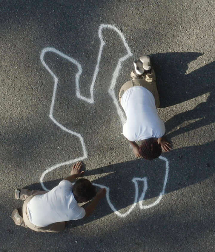 Still from Since I Been Down. Aerial shot of two men kneeling on the concrete, drawing with chalk the silhouette of a human body.