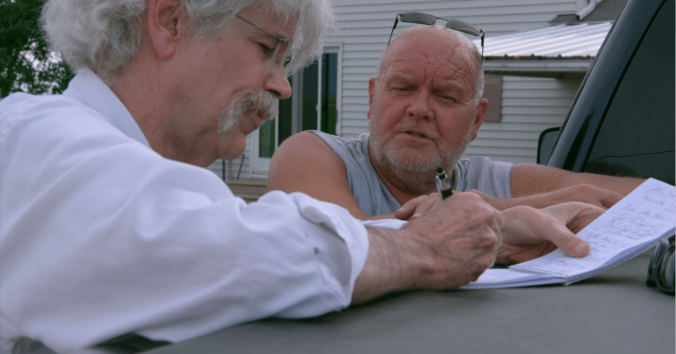 Still from Storm Lake. Art Cullen writes on paper, while other man watches him.