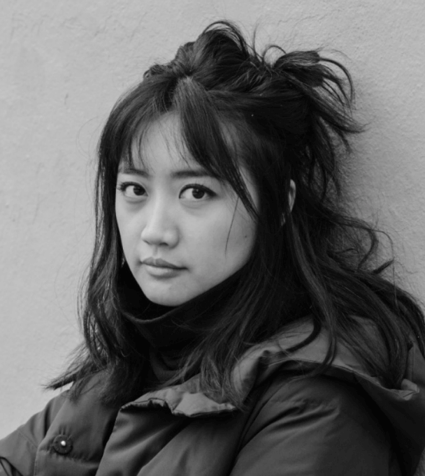 Ash Goh Hua looking straight ahead. She has shoulder-length dark hair partially tied up in a bun. Black and white portrait.