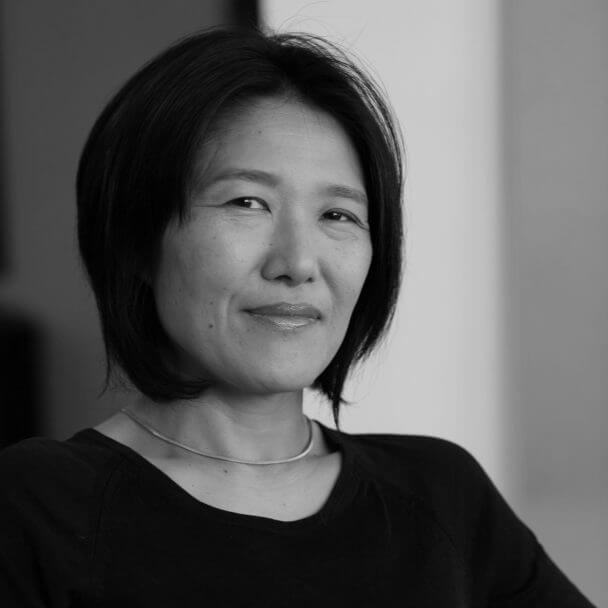 Ann Kaneko smirks while looking directly at the camera. Black and white portrait.