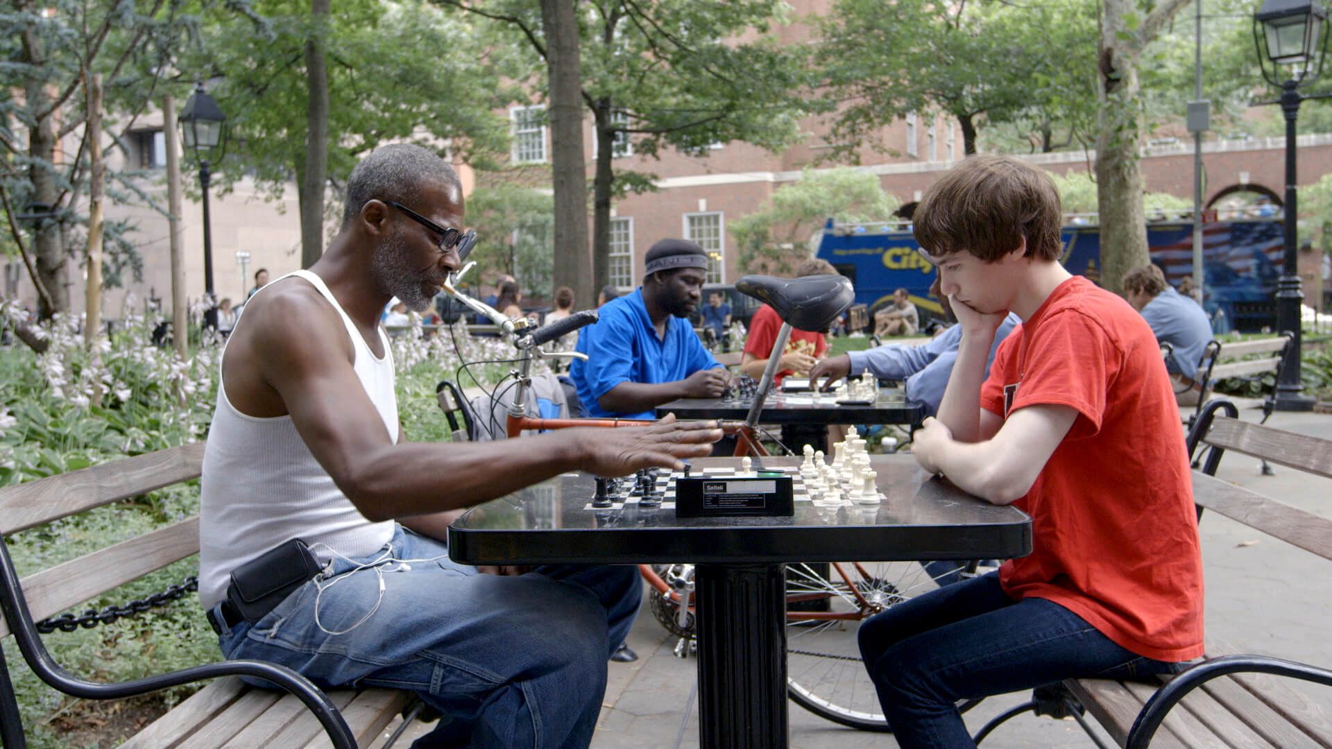 An older Black man and a younger white man study a chess board during a match in Washington Square Park, New York.