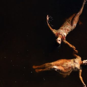 Aerial shot of two women swimming in dark water, wearing nightgowns