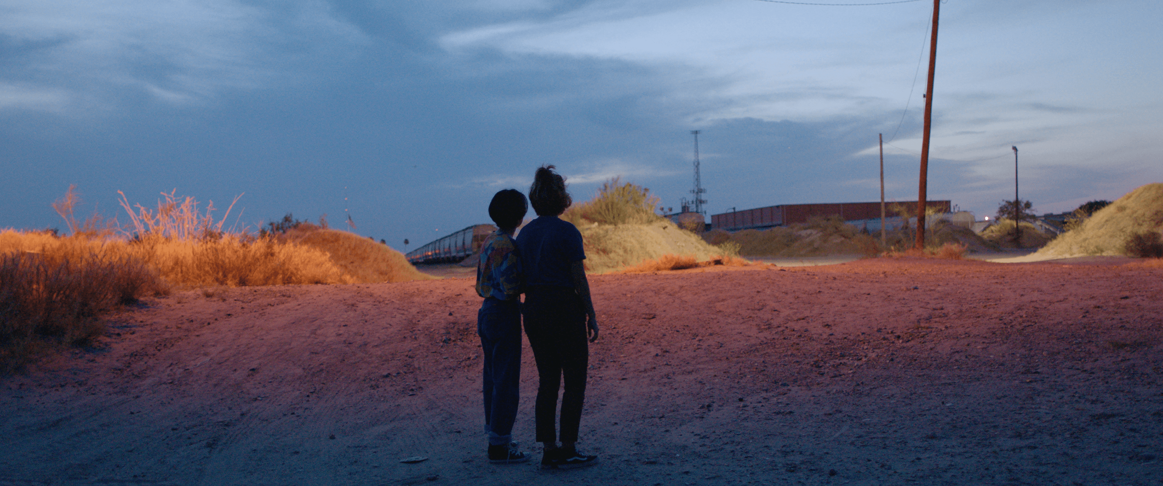 Silvia and Beba's silhouettes are pictured in front of a train at sundown.