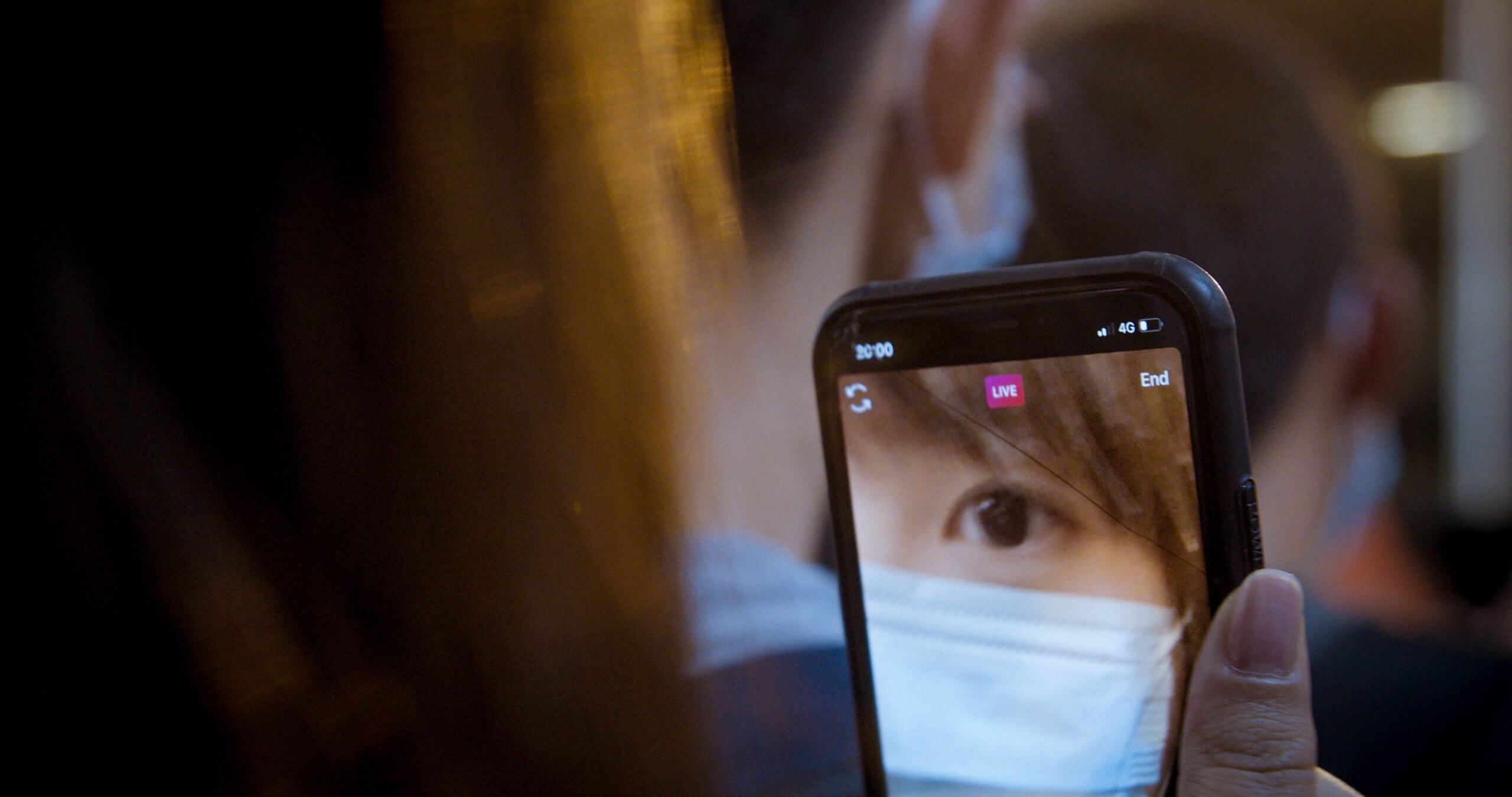 Close up to the screen of a cellphone where we can see the eye of a woman wearing a facemask