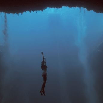 Long shot of a woman in the deep ocean, surrounded