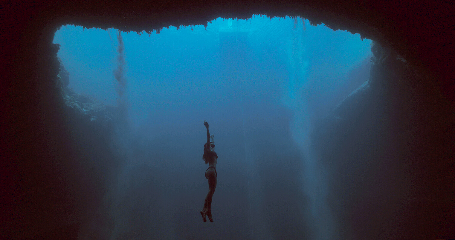 Long shot of a woman in the deep ocean, surrounded