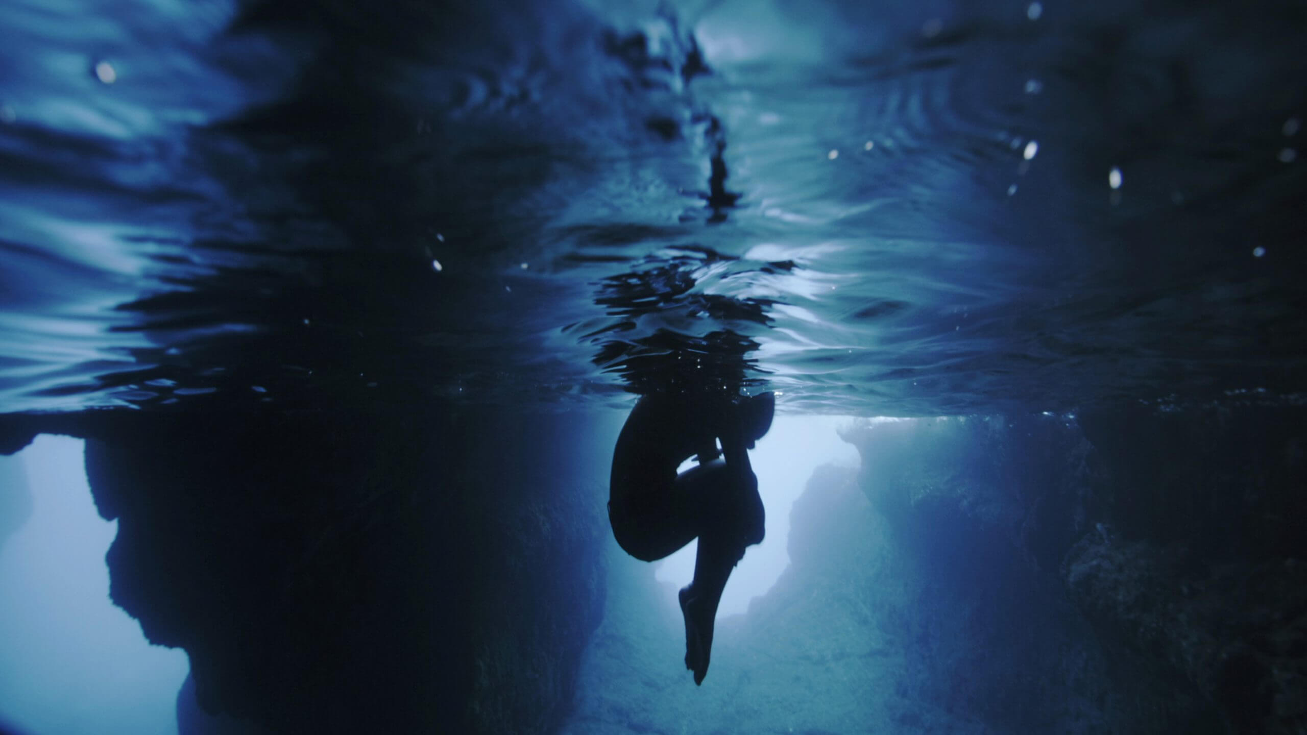 Long shot of a diver clenching her knees under water