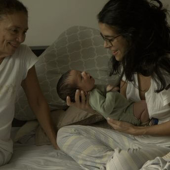 Two women in a bed, one holds a newborn baby and the other watches them
