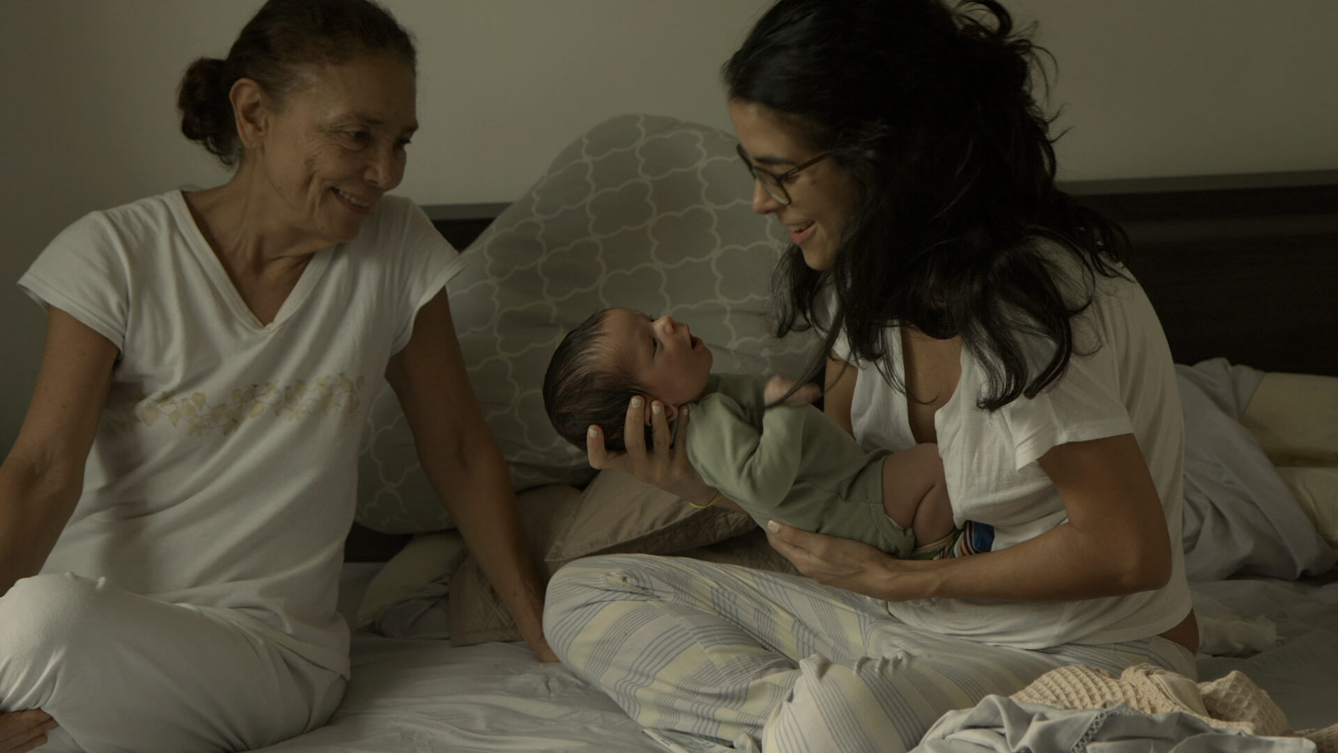 Two women in a bed, one holds a newborn baby and the other watches them