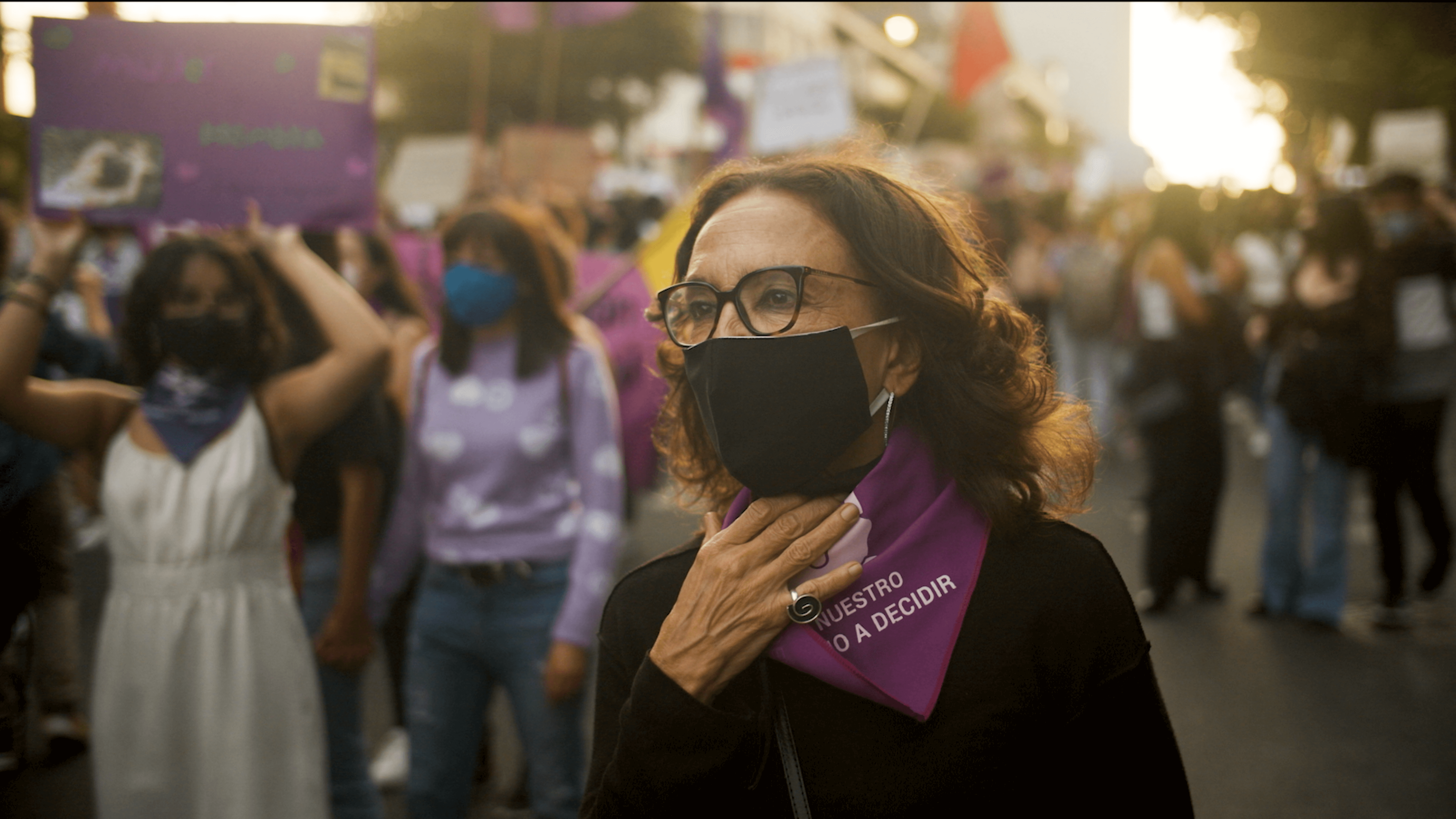 A woman wearing a face mask and a handkerchief knot to her neck, she is in a demonstration