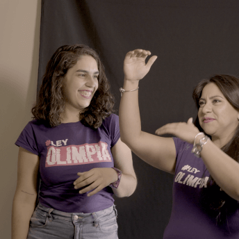 Olimpia Coral and Director Indira Cato laughing during a photoshoot. Both wear a purple "Olimpia Law" t-shirt.