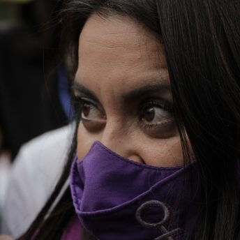 A closeup of Olimpia Coral's face before the Olimpia Law's approval. She wears a purple face mask.