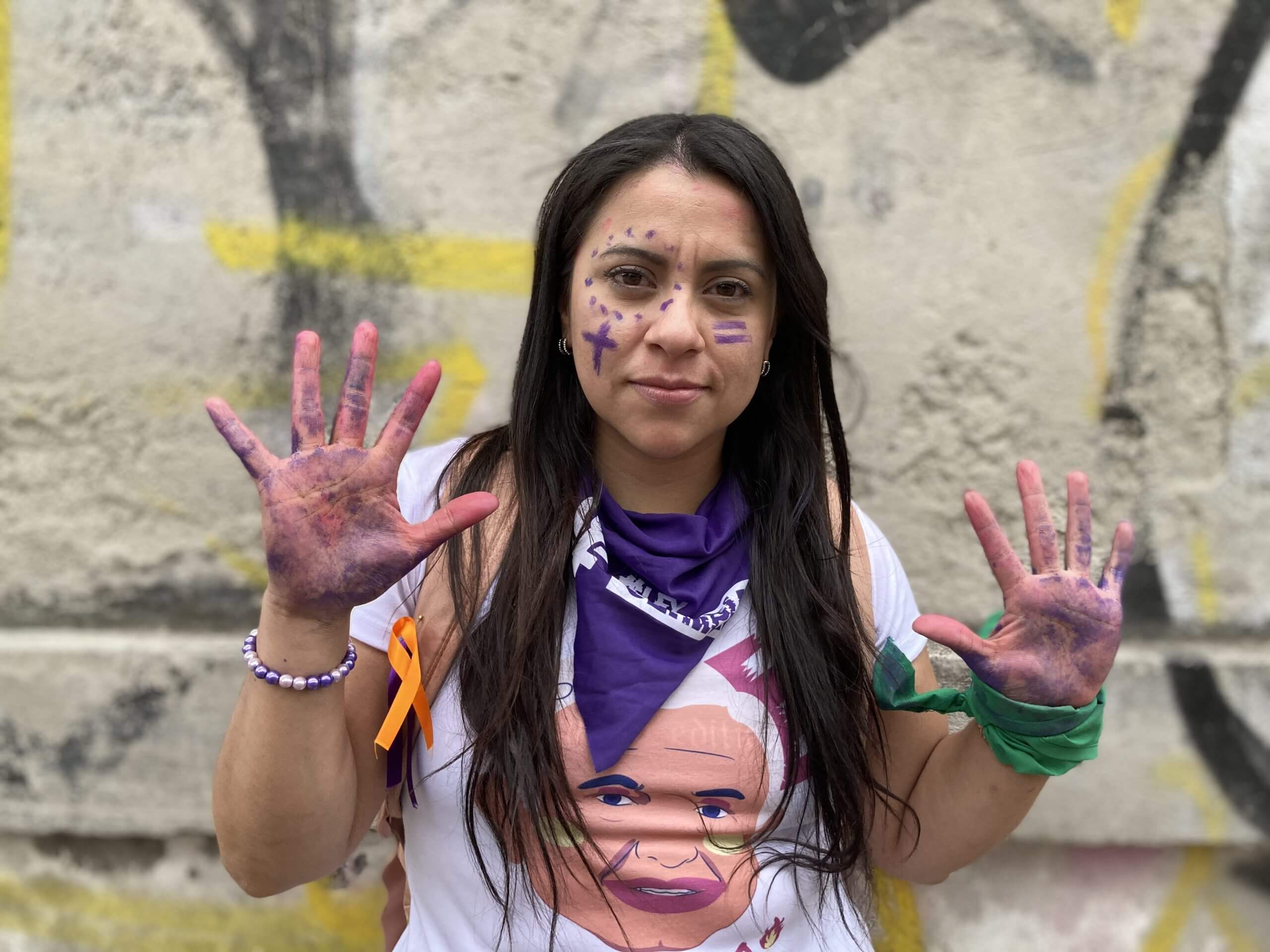 Olimpia Coral Melo after the International Women's Day protest in Mexico City. She shows her face and hands covered in purple marker and wears a purple "Olimpia Law" handkerchief on her neck and a green one on her left wrist.