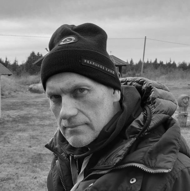 Portrait of a man wearing a hat standing in an open field, he wears a jacket and looks seriously at the camera