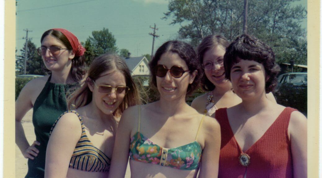 A photograph of 5 women wearing swimsuits and shades, in a sunny day in the '70s.