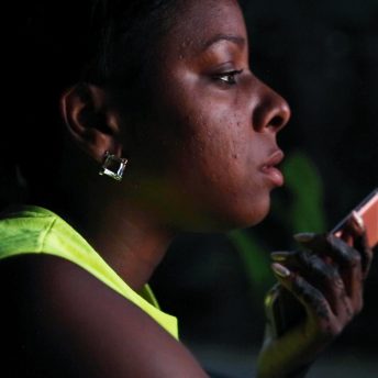 Profile close up shot of a woman holding her cellphone close to her mouth, she wears a fluorescent top