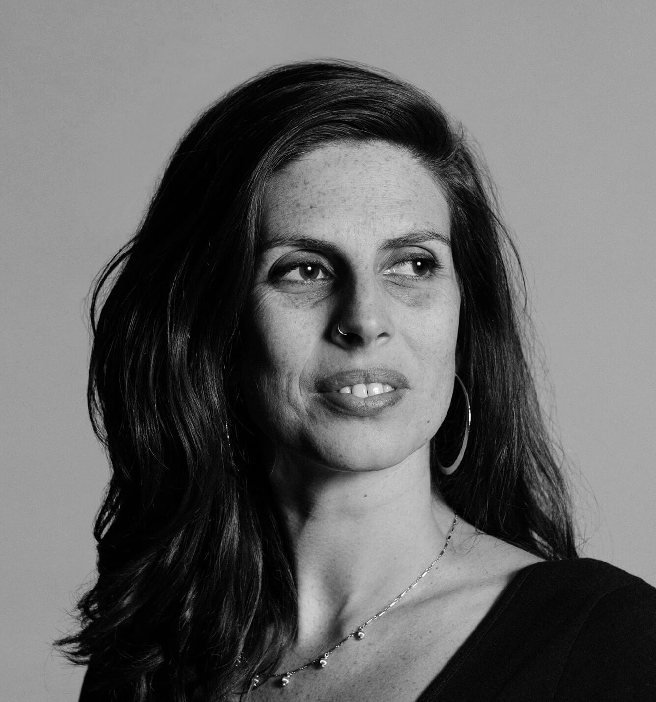 Portrait of Zara Katz, a woman with medium hair, wearing a black shirt with a necklace and looking to the left away from the camera.