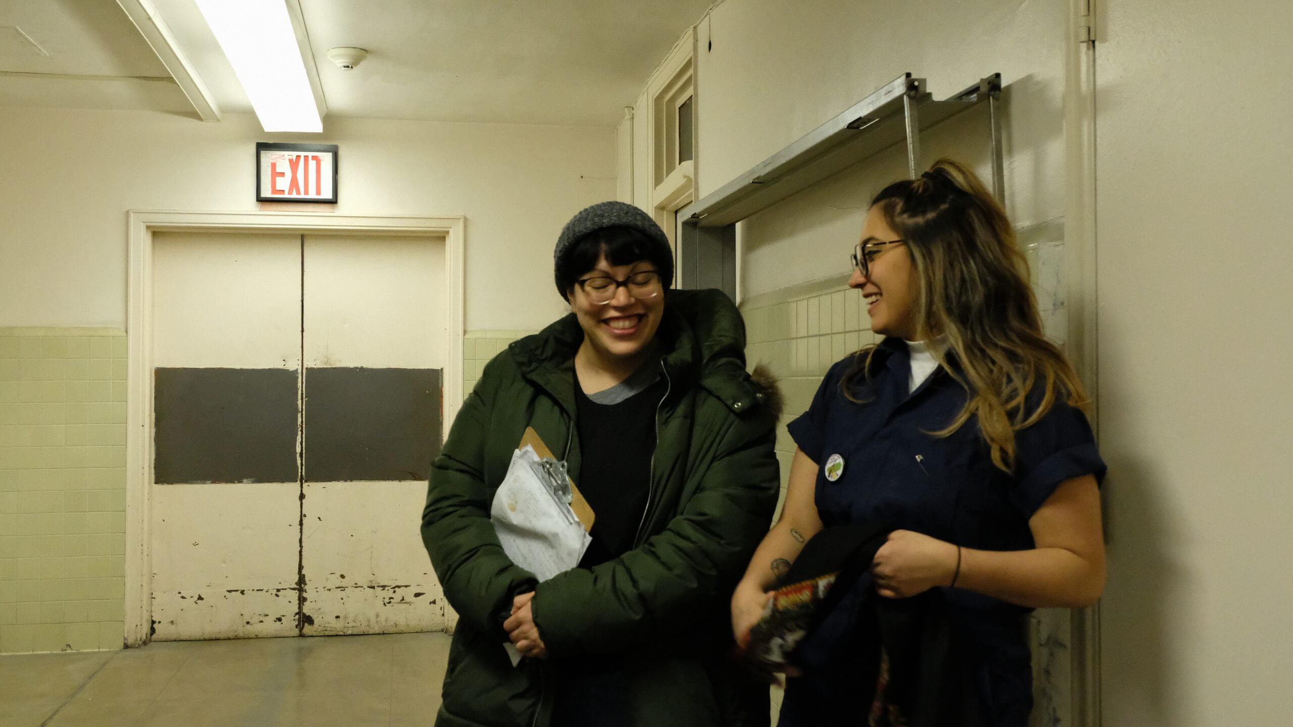 Two women of the production of Takeover talk to each other in a hallway
