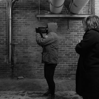 Profile shot of a camera man holding a camera and a woman in a coat behind them