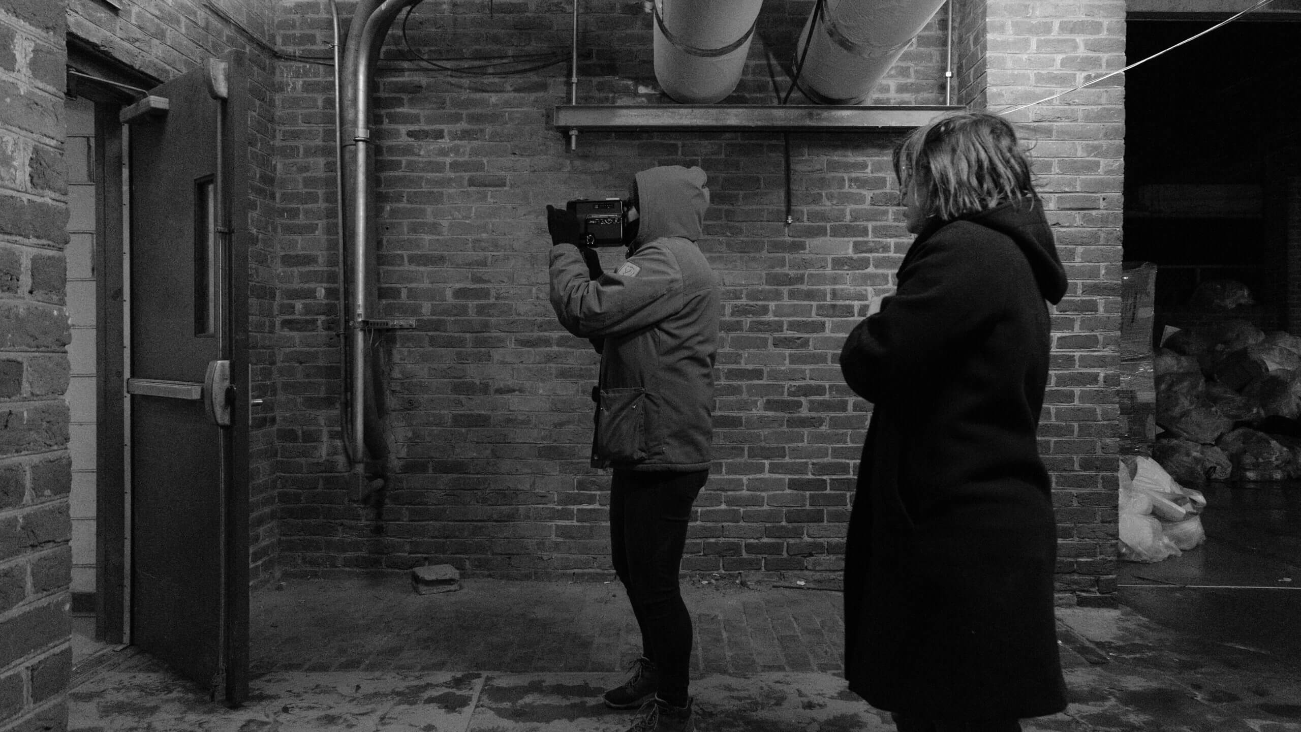 Profile shot of a camera man holding a camera and a woman in a coat behind them